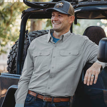 Man wearing grey Crossroad Long Sleeve shirt while leaning against a truck. 