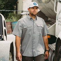 Man wearing grey Crossroad Short Sleeve Shirt while standing outside at a construction site.
