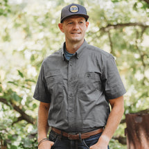 Man wearing gunmetal Craftsman Short Sleeve Shirt stanind outside in woods