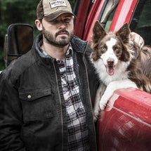 Man wearing Black Endeavor Canvas Jacket standing with dog outside truck.