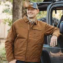 Man wearing saddle Renegade Jacket standing outside leaning agaisnt car