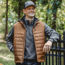 Man wearing saddle Summit Vest standing outside resting arm on fence
