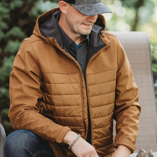 Man wearing saddle heather Pinnacle Puffer Jacket while staring a fire outside