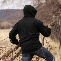Man wearing black River jacket carrying tree branch outside