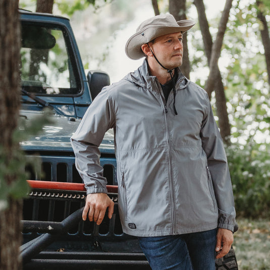 Man wearing grey River jacket standing outside leaning against car
