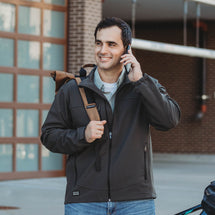 Man wearing charcoal Motion Softshell Jacket standing outside on the phone.