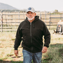 Man wearing black Crossfire Zip Up Hoodie walking outside on farm.