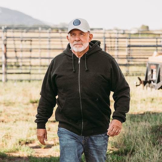 Man wearing black Crossfire Zip Up Hoodie walking outside on farm.
