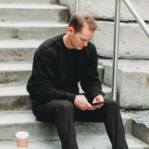 Man wearing black Granite Crewneck sitting outside on stairs