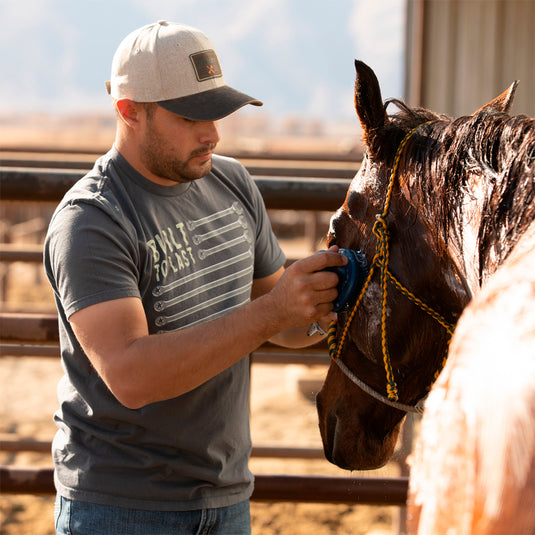 Man wearing charcoal Built to Last Wrench Tee while standing outside with horse